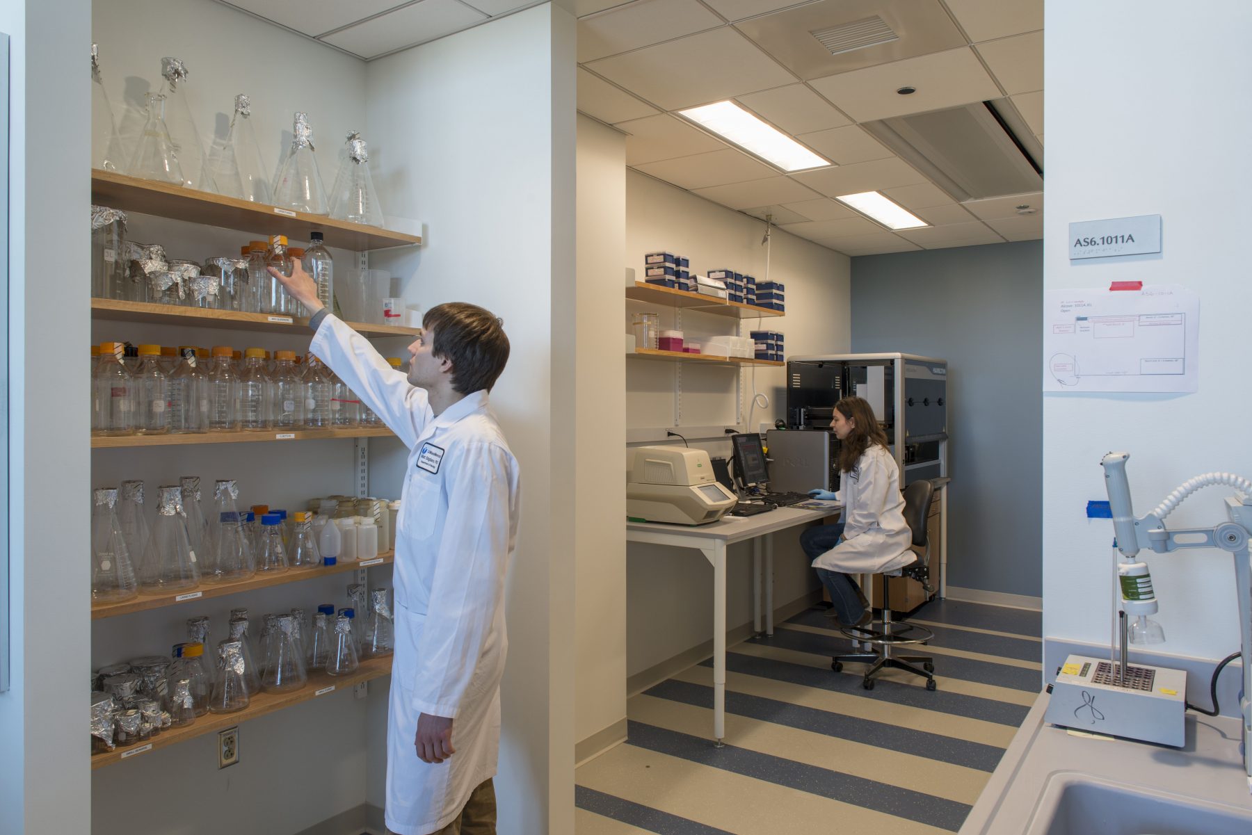 UMass Medical School Sherman Center equipment room, a student retrieves a beaker from a shelf