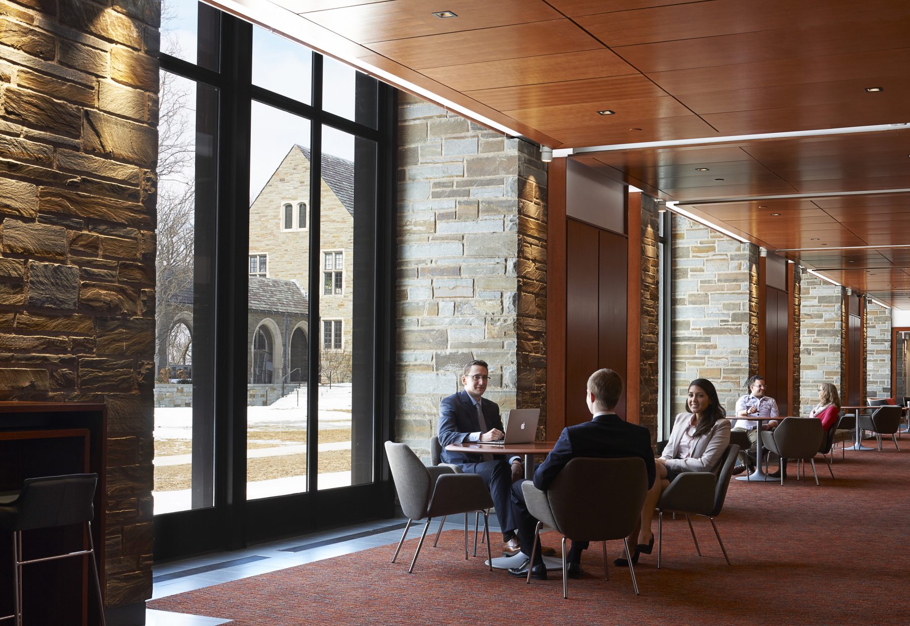 Cornell Law School Hallway, three students sit and socialize around a small circular table.