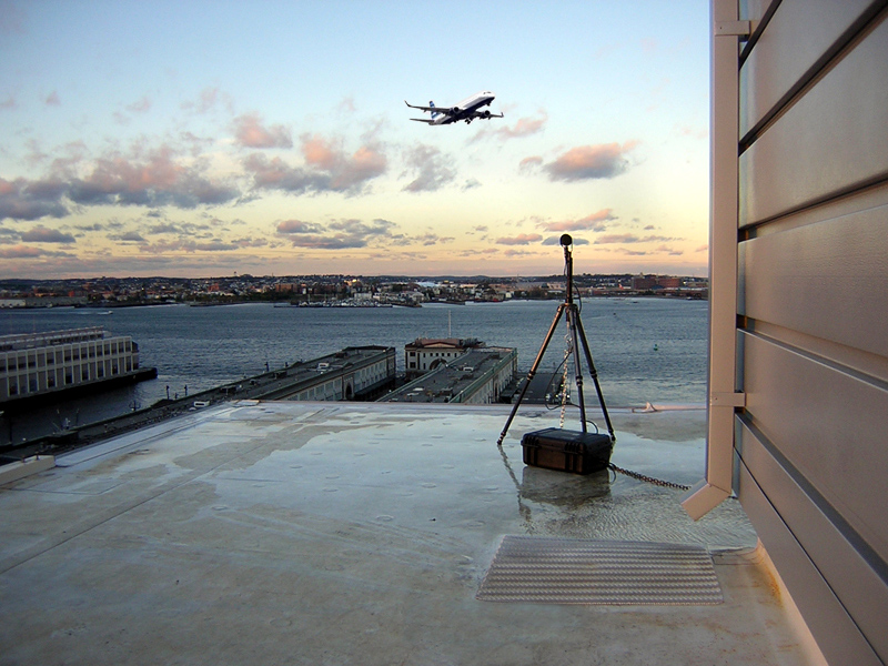 An image of an acoustic measuring microphone on the roof of Park Lane Seaport. An airplane takes off in the background.